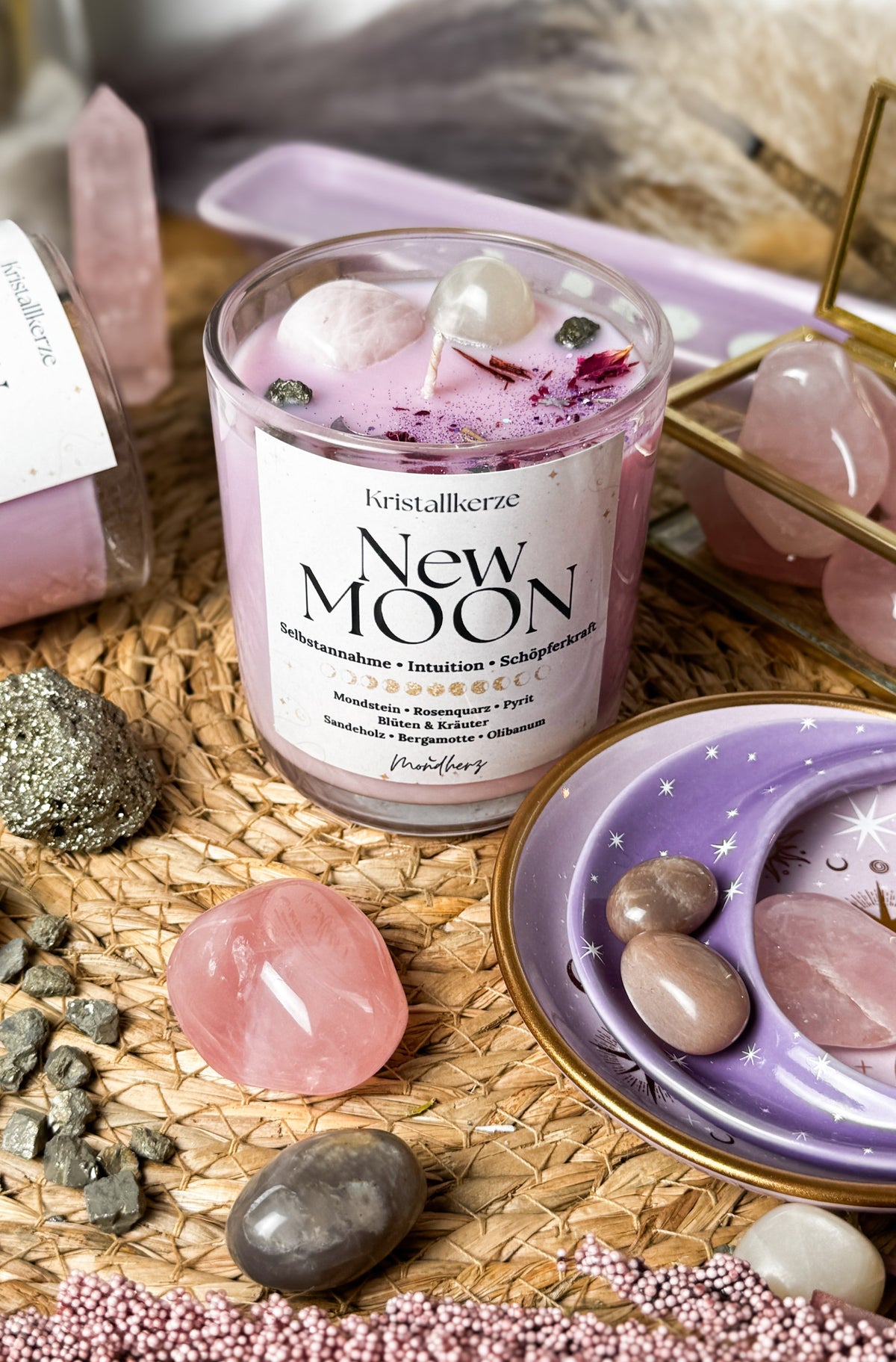 New Moon Kristallkerze von Mondherz mit Rosenquarz, Mondstein, Pyrit und getrockneten Blüten in lila Wachs, umgeben von Heilsteinen und Pampasgras