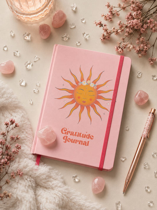 Offenes spirituelles Dankbarkeitstagebuch mit Rosenquarz-Stift auf einem dekorativen Flatlay mit Rosenquarz-Kristallen und Trockenblumen.